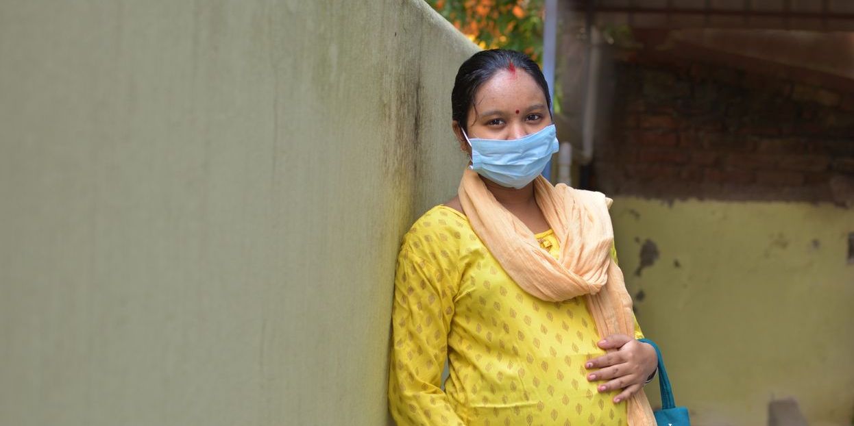 A  pregnant woman in a saari leans against a wall, holding her stomach.