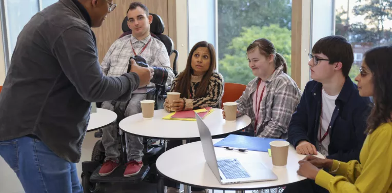 Person talking to group of people with various disabilities sitting at tables